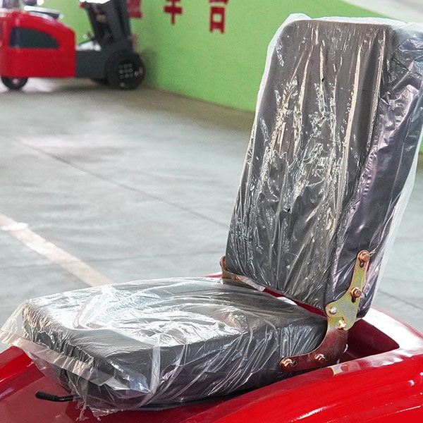 Red electric forklift seat with protective plastic cover in warehouse.